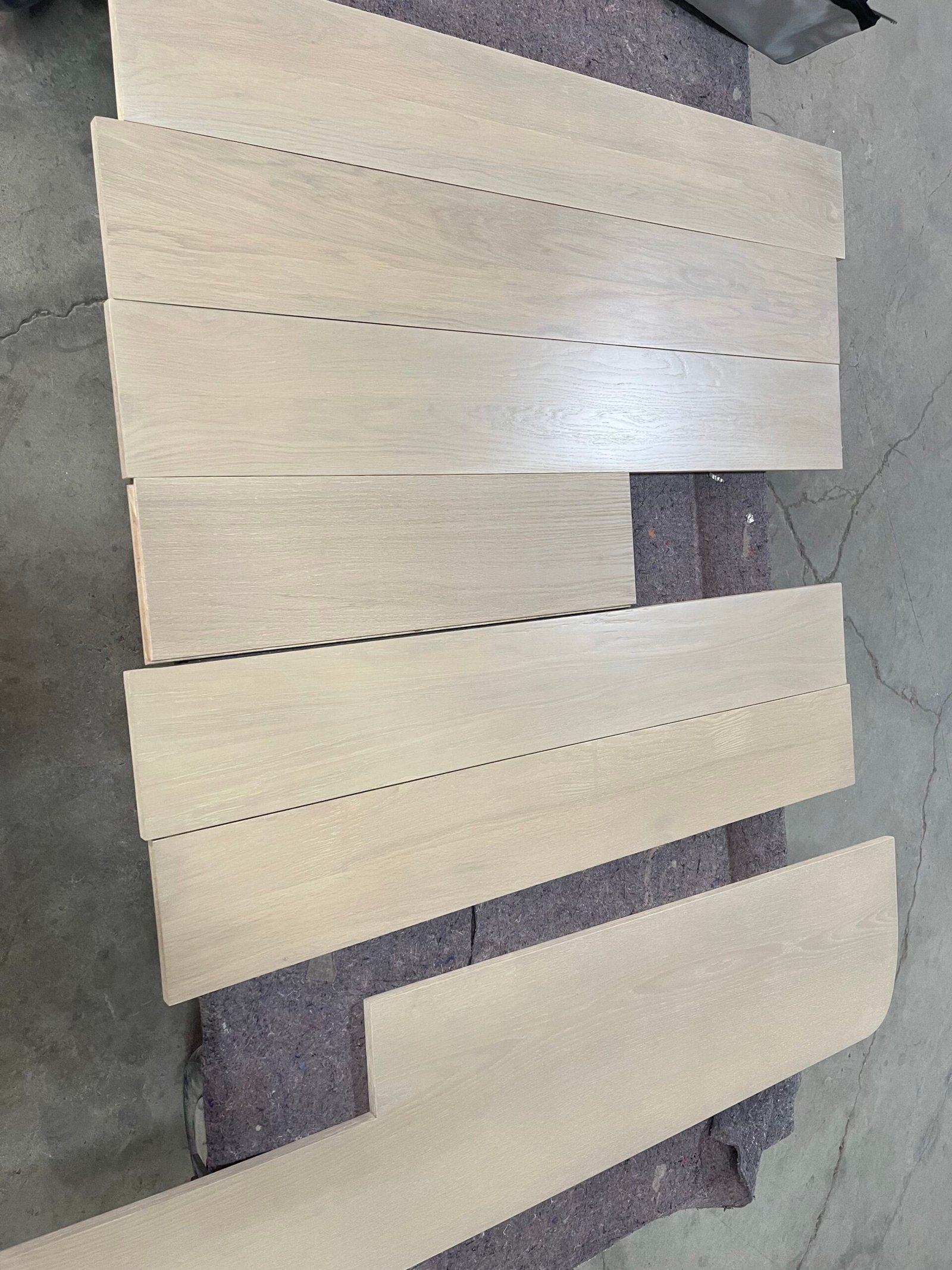 Light-toned red oak stair components laid out on a padded surface, including rectangular and shaped pieces