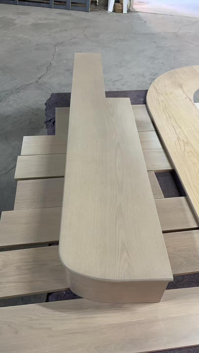 Light-toned red oak stair component with a curved corner and downward front edge, resting above boards