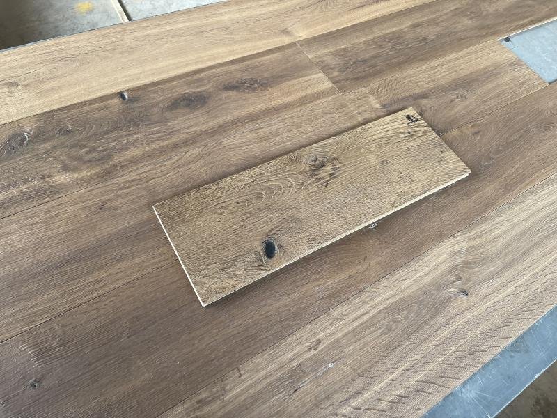 Rectangular oak flooring sample resting across larger boards, showing textured grain and visible knots