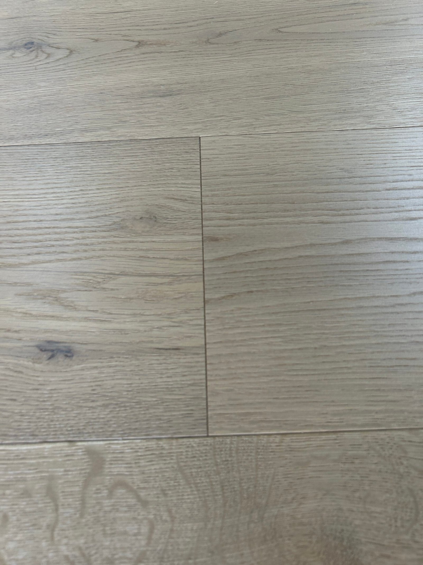 Close-up of Stone Greige oak flooring showing grain lines, small knots, tonal variation, and board joints